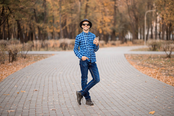 young stylish bearded man in sunglasses listening to music in fall - Photo, Image