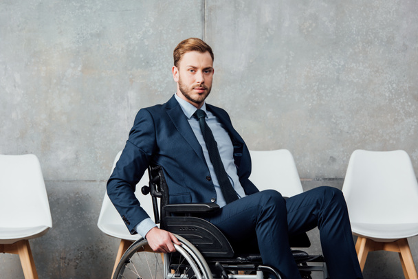 handsome businessman sitting in wheelchair in waiting hall and looking at camera - Foto, Bild