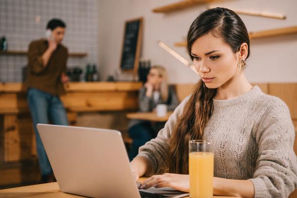 mujer grave escribiendo en el ordenador portátil mientras está sentado en la cafetería
 - Foto, imagen