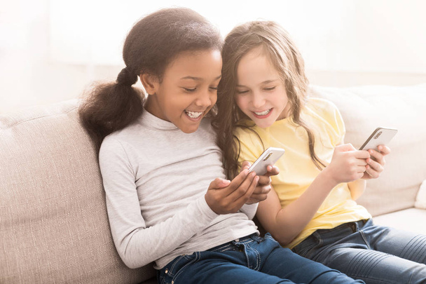 Happy little friends with smartphones sitting on sofa - Photo, Image