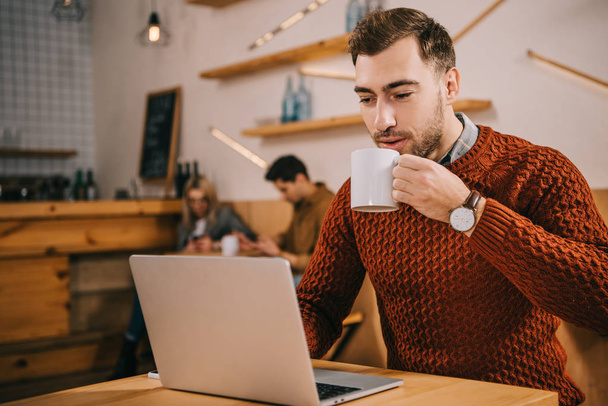hombre guapo bebiendo café y mirando el ordenador portátil en la cafetería
 - Foto, imagen