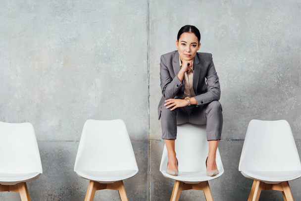 schöne asiatische Geschäftsfrau in formeller Kleidung sitzt auf einem Stuhl und schaut in die Kamera in der Wartehalle - Foto, Bild