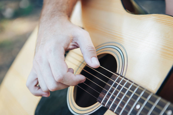 Lähikuva miehen kädestä soittamassa kitaraa. Mies soittaa kitaraa. Soittaminen akustinen kitara ulkona
 - Valokuva, kuva