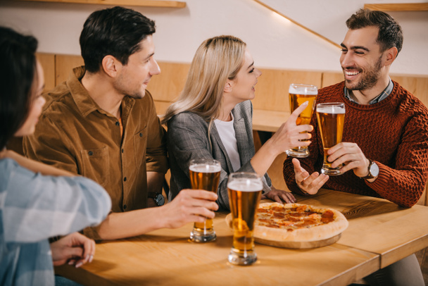 selective focus of cheerful friends toasting glasses of beer in bar - Фото, изображение