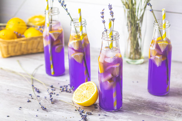 Свежий лавандовый фиолетовый коктейль с лимоном и льдом, стакан для питья бутылок на светлом старом деревенском стиле, выборочная фокусировка, мелкая глубина поля
. - Фото, изображение