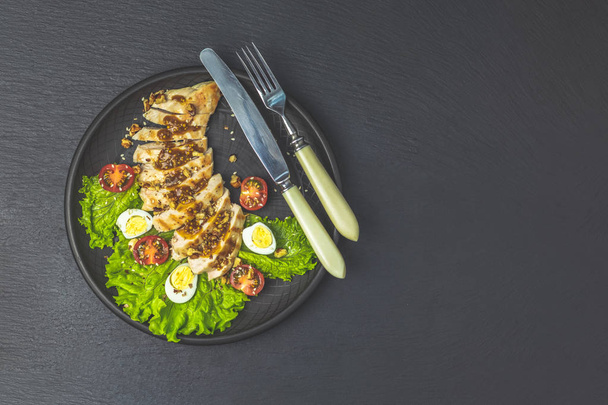 Heerlijke salade kip met honing en mosterd saus, sla, kwarteleitjes, cherrytomaatjes en sesam in zwarte keramische plaat, bovenaanzicht, kopie ruimte, hawaiian, Aziatische gerechten. - Foto, afbeelding