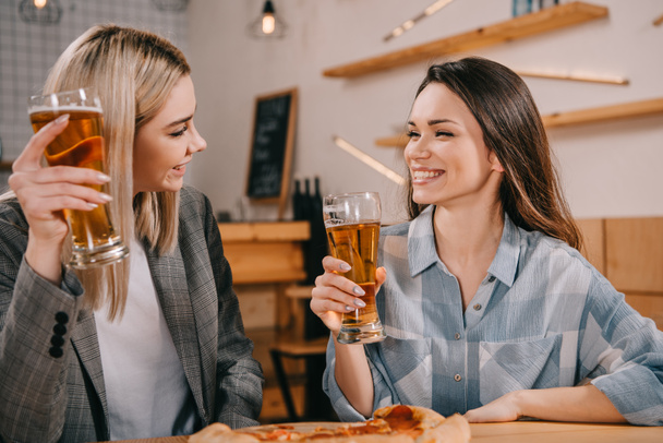 attractive friends smiling while holding glasses of beer in bar - Foto, immagini