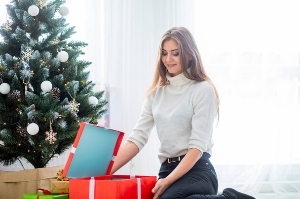 Young woman in front of Xmas tree opening Christmas gifts - Foto, immagini