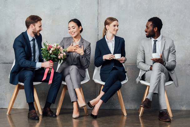 multiethnic businesspeople sitting with flowers and coffee in office - Foto, imagen