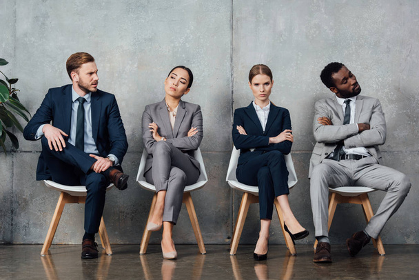 empresários multiétnicos insatisfeitos sentados em cadeiras com braços cruzados na sala de espera
 - Foto, Imagem