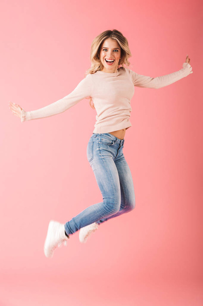 Full length portrait of a happy young woman wearing sweater jump isolated over pink background - Fotoğraf, Görsel