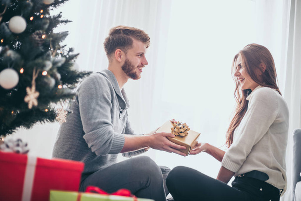 Happy couple in love celebrating Christmas together at home next to Xmas tree - Zdjęcie, obraz