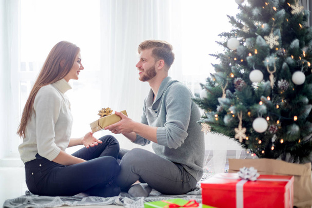 Happy couple in love celebrating Christmas together at home next to Xmas tree - Foto, Imagem