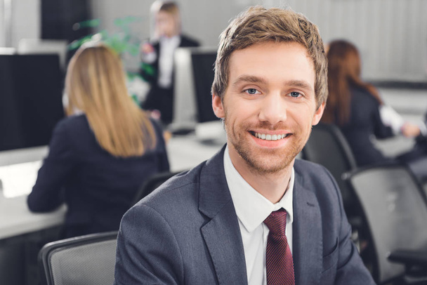 portrait of handsome young businessman smiling at camera in open space office - 写真・画像