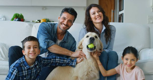 Portrait of happy family with a dog having fun together in living room. Concept of happy family, love for animals, childhood - Foto, imagen