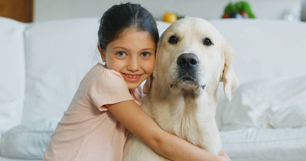 Πορτρέτο pf κοριτσάκι παίζει και αγκαλιάζοντας το σκύλο της στο σαλόνι. Έννοια της αγάπης για τα ζώα, παιδική ηλικία, σκύλος pedigree - Φωτογραφία, εικόνα