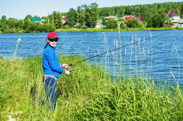  woman with a spinning rod catches a fish in the lake in summer day - Φωτογραφία, εικόνα