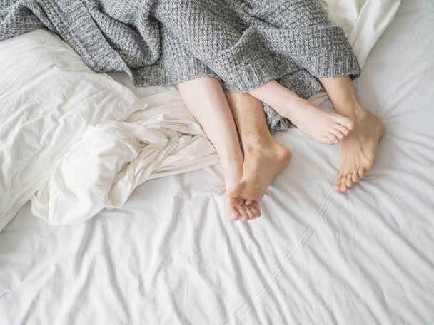Nahaufnahme männlicher und weiblicher Füße auf dem Bett - Liebespaar unter grauer Decke im Schlafzimmer - Konzept des sinnlichen und intimen Moments der Liebenden. - Foto, Bild