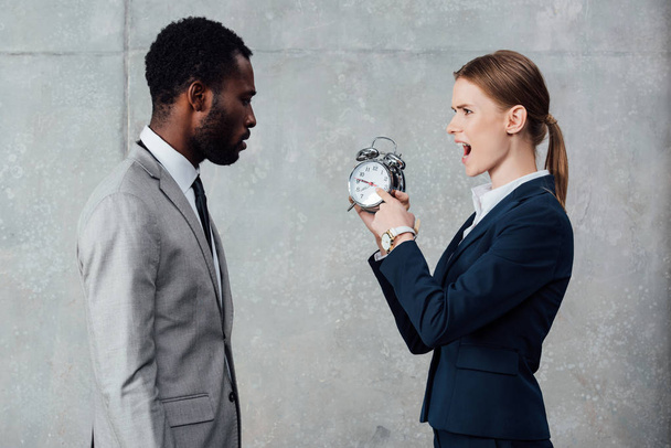 african american businessman looking at yelling businesswoman pointing at clock on grey background - Foto, afbeelding