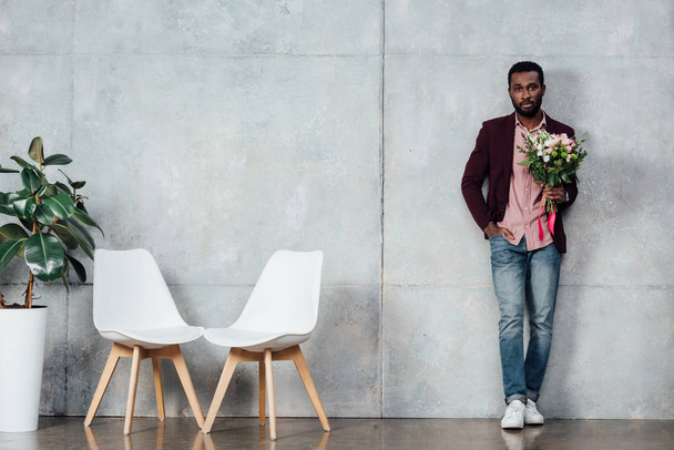 african american man in casual clothes holding flowers in waiting hall - Foto, Imagen
