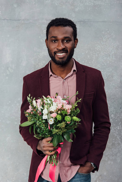 african american man in casual clothes holding flowers and looking at camera on grey background - Foto, imagen