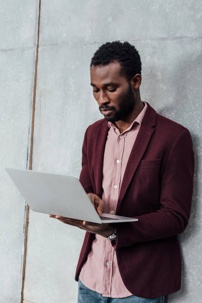 focused african american casual businessman using laptop on grey background - Фото, зображення