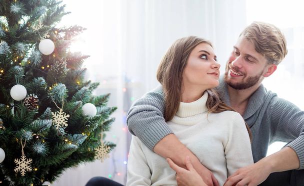 Couple celebrating Christmas together, sitting on floor next to Xmas tree - Foto, Imagem