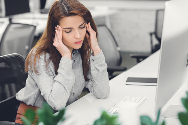 young businesswoman with closed eyes suffering from headache at workplace - Zdjęcie, obraz