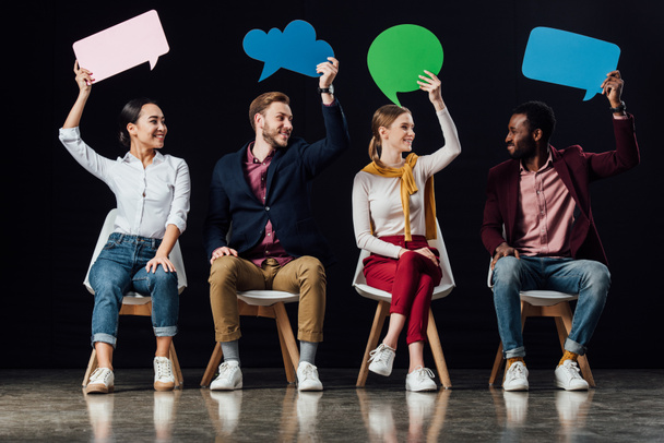 happy multiethnic people holding speech bubbles and thought bubble isolated on black - Фото, зображення
