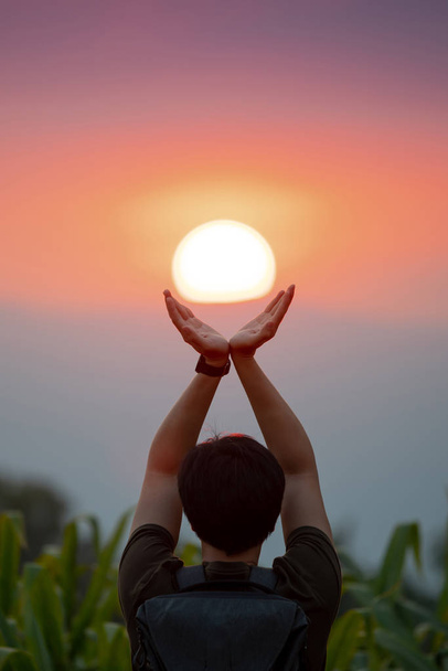 Hombre asiático en el campo de maíz levantando los brazos sosteniendo el sol al atardecer. Esperanza y oración. Concepto de logro
 - Foto, Imagen