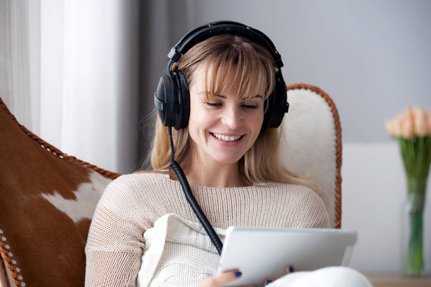 Young woman at home wearing headphones while using digital tablet, watching movie online or browsing internet - Fotó, kép