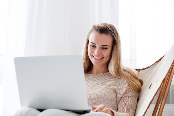 Woman sitting in cozy armchair and using laptop, working online at home - Foto, Imagem