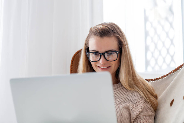 Žena sedí v útulné křeslo a pomocí přenosného počítače, práce doma online - Fotografie, Obrázek