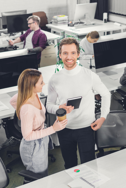 high angle view of happy businesswoman with coffee to go and smiling businessman standing together in office - Foto, immagini