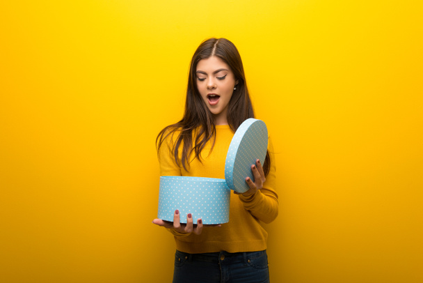 Adolescente sur fond jaune vibrant tenant boîte cadeau dans les mains
 - Photo, image