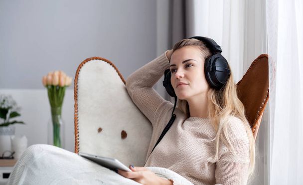 Woman at home wearing headphones while using digital tablet, listening to audiobooks or music - Foto, afbeelding