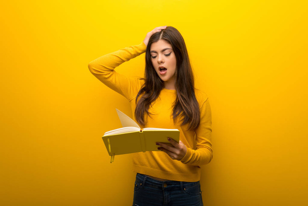 Teenager girl on vibrant yellow background surprised while enjoying reading a book - Foto, Imagem