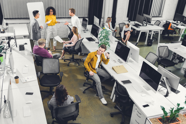 Blick aus der Vogelperspektive auf junge Geschäftskollegen, die im Großraumbüro mit Papieren und Computern arbeiten    - Foto, Bild