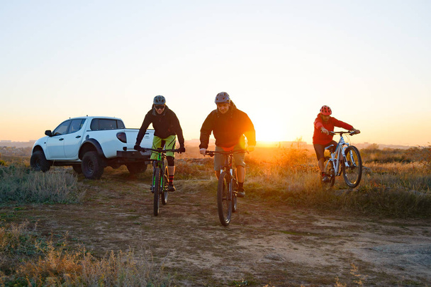 Friends Cyclists Riding Enduro Bikes in the Mountains in front of the Pickup Off Road Truck at Warm Autumn Sunset. MTB Adventure and Car Travel Concept. - Fotó, kép