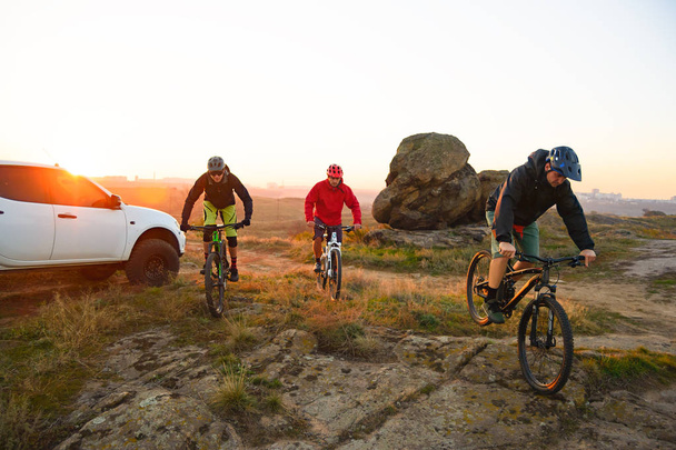 Friends Cyclists Riding Enduro Bikes in the Mountains in front of the Pickup Off Road Truck at Warm Autumn Sunset. MTB Adventure and Car Travel Concept. - Fotó, kép
