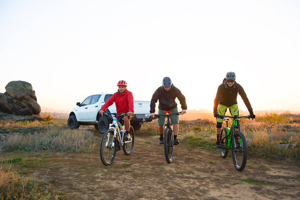 Friends Cyclists Riding Enduro Bikes in the Mountains in front of the Pickup Off Road Truck at Warm Autumn Sunset. MTB Adventure and Car Travel Concept. - Photo, Image