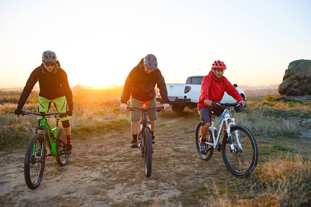 Friends Cyclists Riding Enduro Bikes in the Mountains in front of the Pickup Off Road Truck at Warm Autumn Sunset. MTB Adventure and Car Travel Concept. - Foto, Imagem