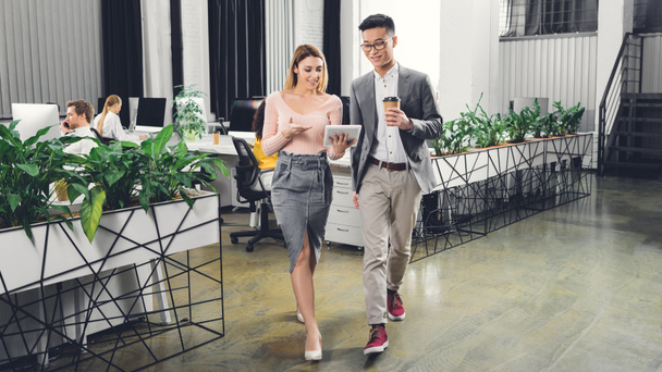 feliz profesional jóvenes colegas de negocios utilizando tableta digital y caminando en la oficina
  - Foto, imagen