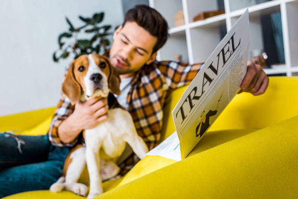 selective focus of happy man reading travel newspaper while sitting on sofa with beagle dog - Photo, image