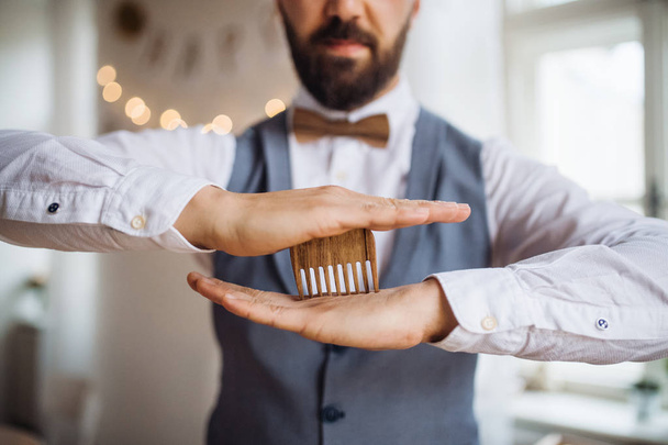 Midsection of man standing indoors in a room set for a party, holding a beard comb. - Foto, Bild