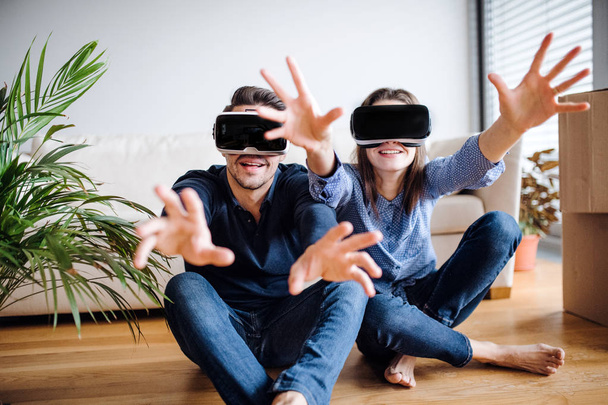 A young couple with VR goggles sitting on a floor, moving in a new home. - Fotografie, Obrázek