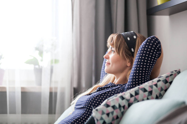 Onnellinen nuori nainen istuu sohvalla rentouttava kotona, haaveilee ja ajatella jotain vapaa-ajalla
 - Valokuva, kuva