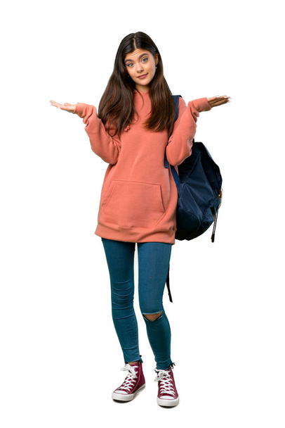 A full-length shot of a Teenager girl with sweatshirt and backpack having doubts while raising hands and shoulders - Photo, Image