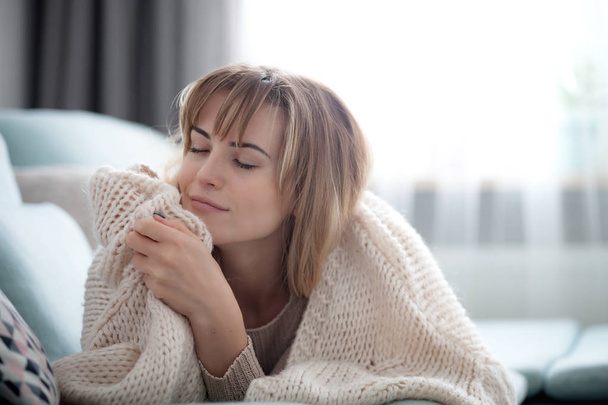 Happy young woman hugging soft knitted sweater, relaxing on sofa at home - Fotó, kép