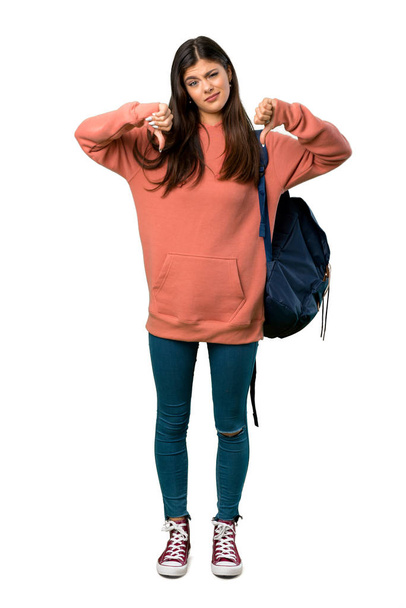 Una foto completa de una adolescente con sudadera y mochila mostrando el pulgar hacia abajo con ambas manos
 - Foto, Imagen